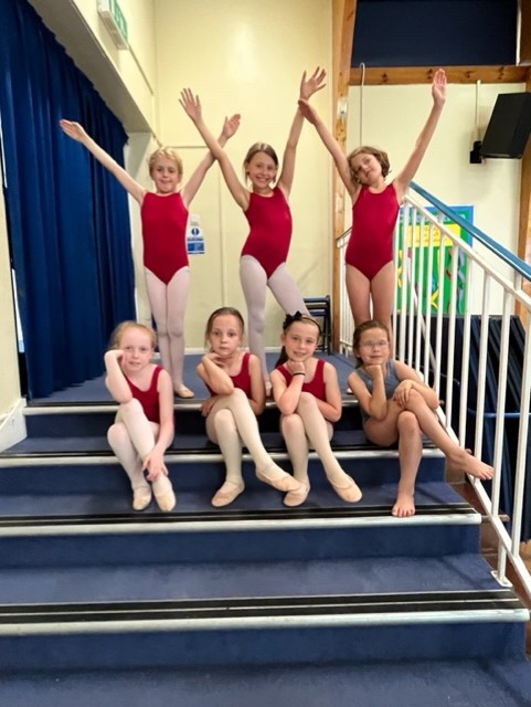 school children facing away in red ballet leotards standing and posing to the right. 
