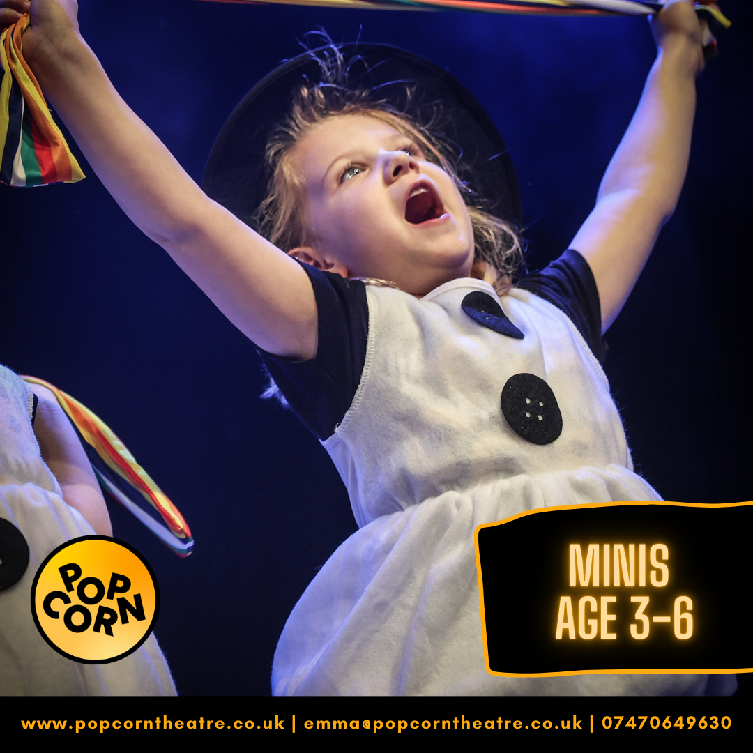 A 6yr old girl with blonde hair singing with her hands in the air wearing a white dress with very large black buttons and wide capped sleves in black