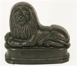 A CAST-IRON FIRE ORNAMENT crudely formed as a recumbent lion^ resting on a rounded rectangular
