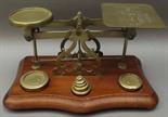 A brass postal balance with six stacking weights on a shaped walnut base.