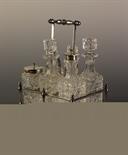 A Six-bottled Silver-plated Cruet Set. The cut glass bottles in a rectangular stand with beaded