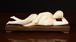 An 18th Century Oriental Ivory Carving of a naked lady reclining on a hardwood stand, 9½ ins (24