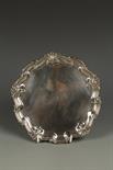 AN EDWARDIAN SALVER of circular form, with raised scroll and shell border, on three scroll feet,