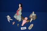 A 1920's porcelain doll pin cushion, ceramic model of a seated girl, porcelain cake decoration,