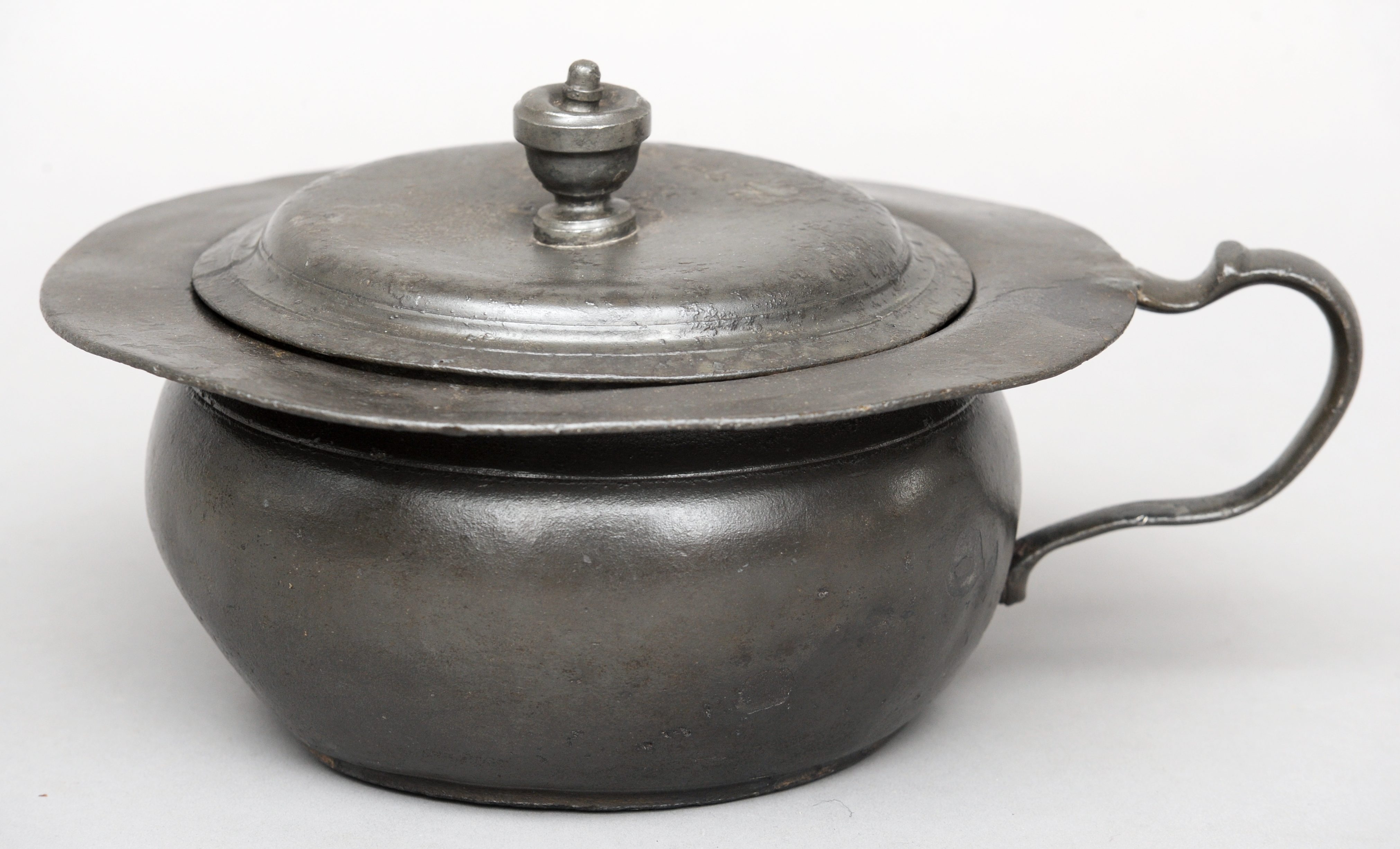 An 18th century pewter lidded chamber pot Of typical form, with loop