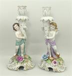 A pair of German porcelain figural candlesticks modelled with cherubs, raised on rococo scroll bases