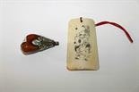 A BONE PENDANT
etched with a Buddha and another amber type pendant with white metal mount. (2)