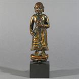 A FIGURE OF A MONK: Tibet, 16th century gilt wood, with traces of green paint, standing on a lotus