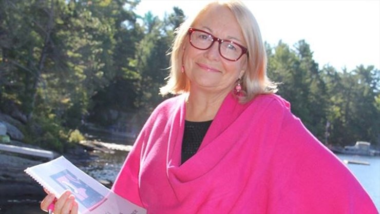 Sue Kelly author and speaker standing with book in front of lake