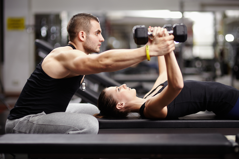 woman lifting weights with male spotter