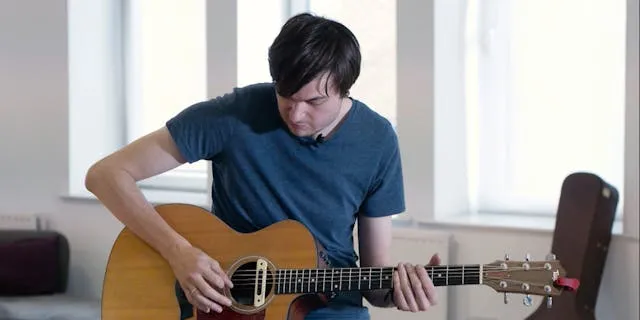 A man playing an acoustic guitar and tuning it
