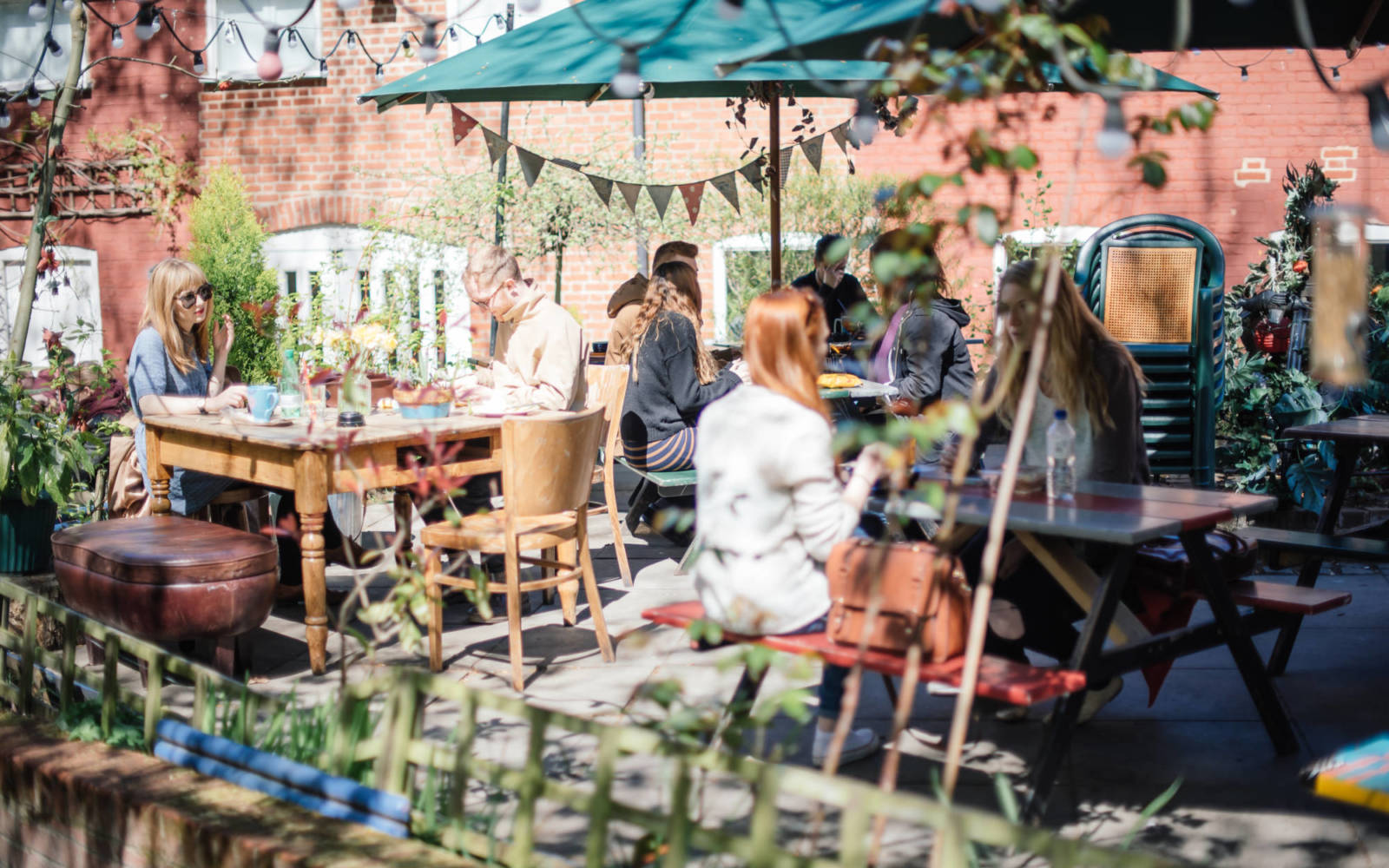 Photo of the Norwich Playhouse bar courtyard on a sunny day. People are sitting at picnic benches,