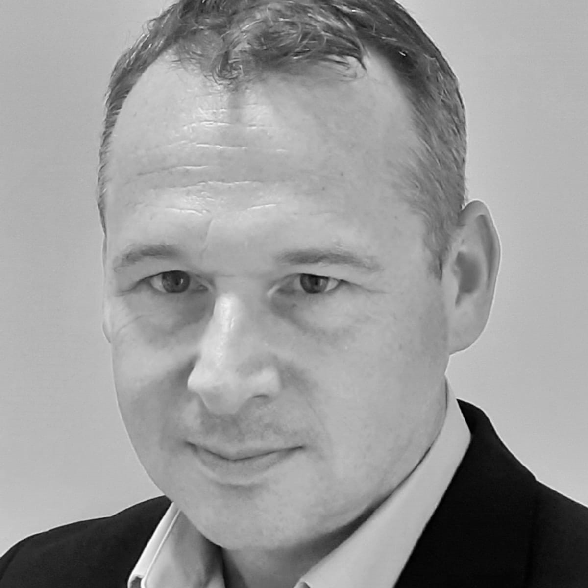 Tim-Ochala-Greenough A man with short hair wearing a shirt under a suit jacket.