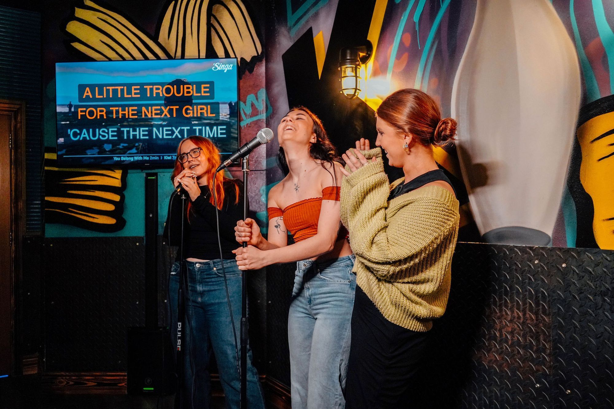 3 junge Frauen performen Karaoke in einer Karaoke-Bar.