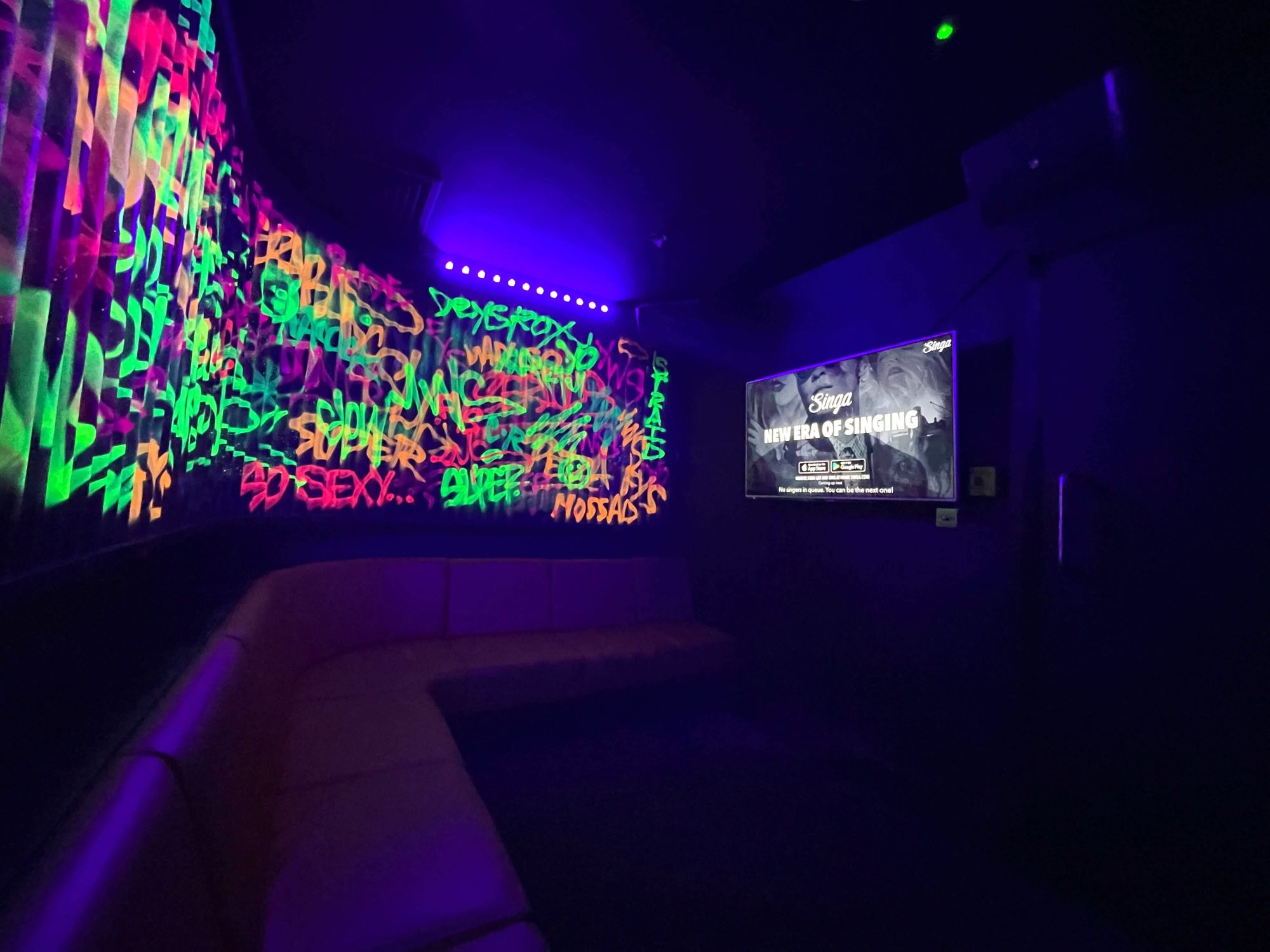 Karaoke-Raum mit Schwarzlicht und Neongraffiti an den Wänden.