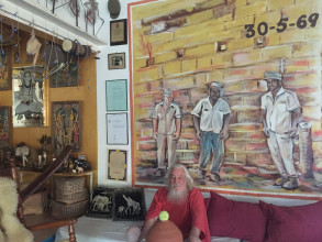 Portret Stanley Brown in zijn woning voor een werk van kunstenaar Jean Girigori met daarop leiders van de 30 mei-opstand: vanaf links Stanley, Papa Godett en Amadornita. Foto: Stephanie Archangel.