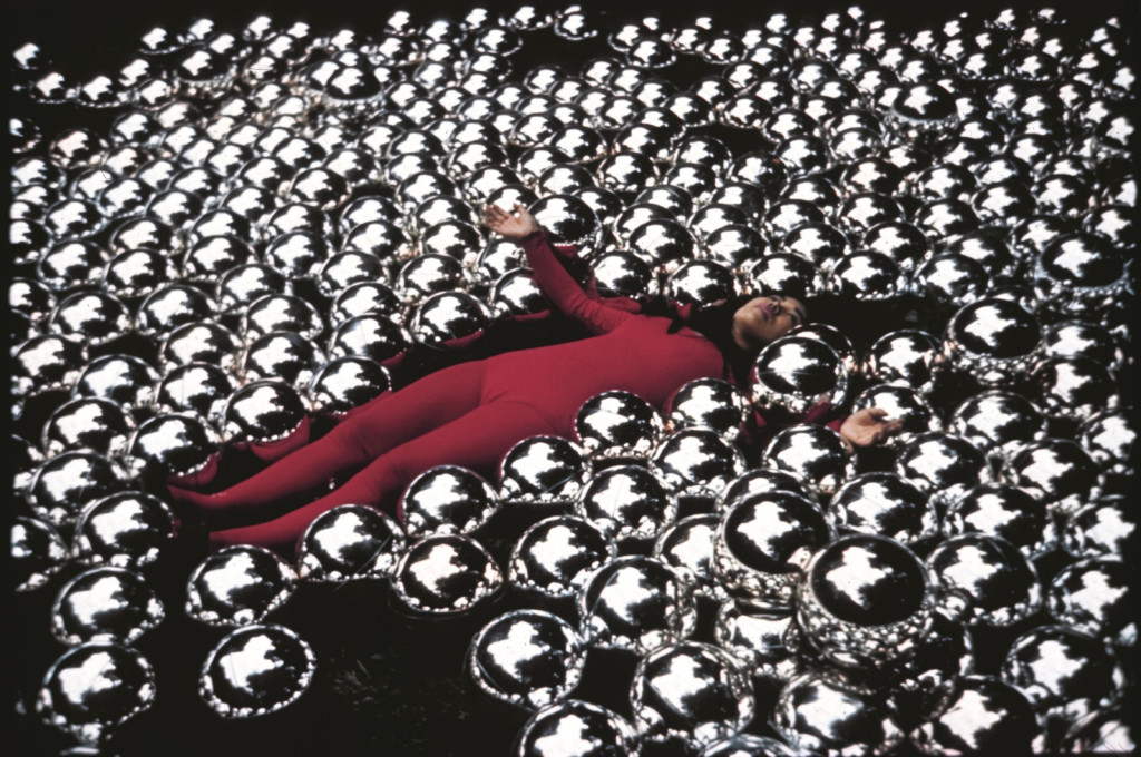 photo of yayoi kusama in her installation Narcisssus Garden, space filled with metal balls