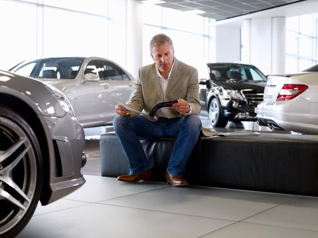 Man reading brouchure surrounded by shiny new cars in car dealership