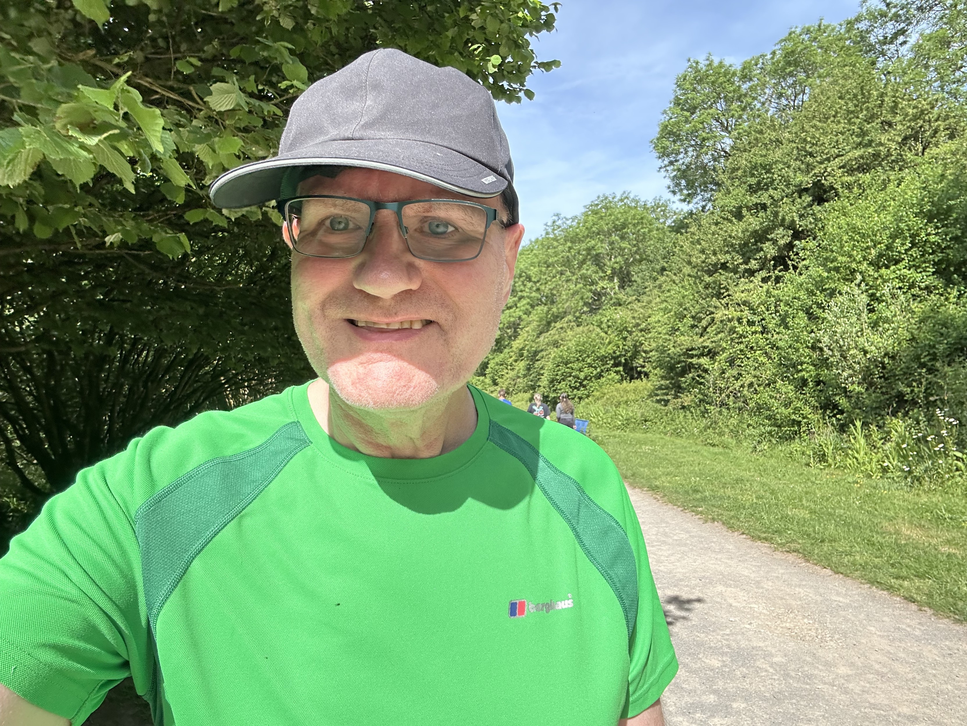 Selfie en route, I’m in a black running cap and green shirt, in front of a path with trees on both sides 