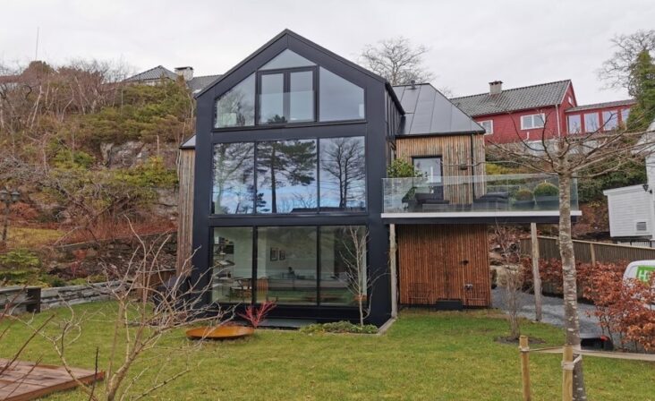 Enebolig med trepanel og iøynefallende gavlvegg av glass og aluminium fra Schüco, levert av Gjesdal Aluminium AS sett fra hagen.