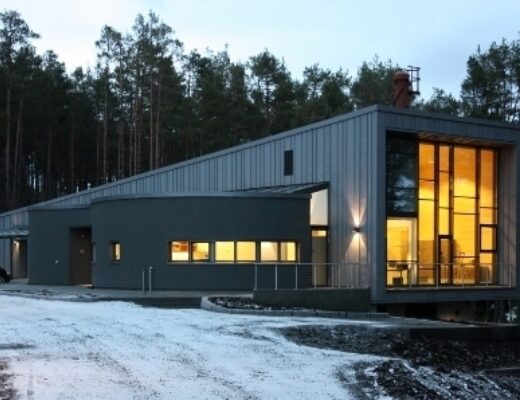 Ålesund krematorium om kvelden med stor, opplyst Schüco-glassfasade på frontveggen, delt inn i flere ruter av ulik størrelse.