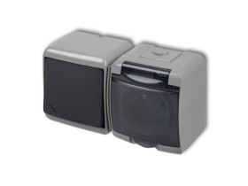 JUNIOR IP54 Wyłącznik schodowy z gniazdem pojedynczym z uziemieniem (klapka dymna: przesłony torów prądowych) popielaty / grafit