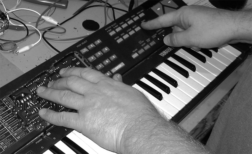 Mike Challis playing his hacked Yamaha PS-140 by touching the circuit board through a hole cut through the case