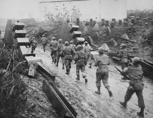 American soldiers stream past Siegfried Line defenses