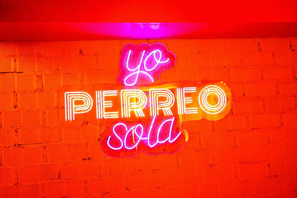 Letrero de ne&oacute;n "Yo perreo sola" en una pared de ladrillo iluminada en rojo dentro de Pizpireta Bar
