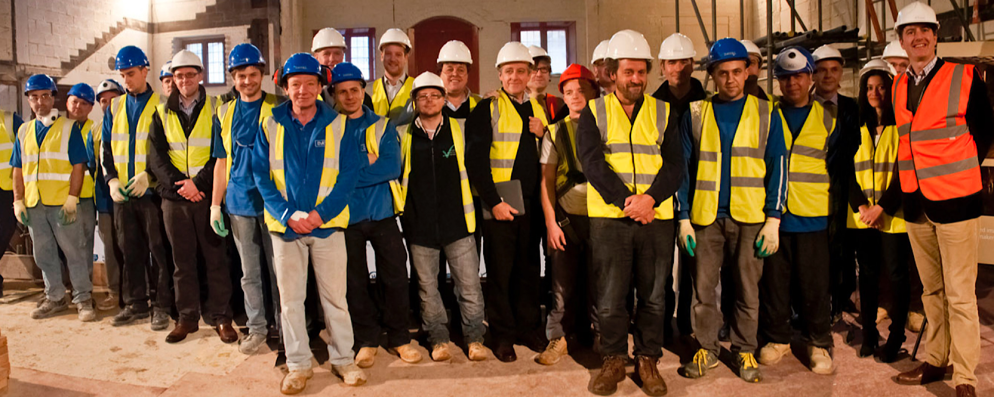 Sam Wanamaker Playhouse Construction A large group of people in high visibility jackets and hard hats stand on an indoor construction site