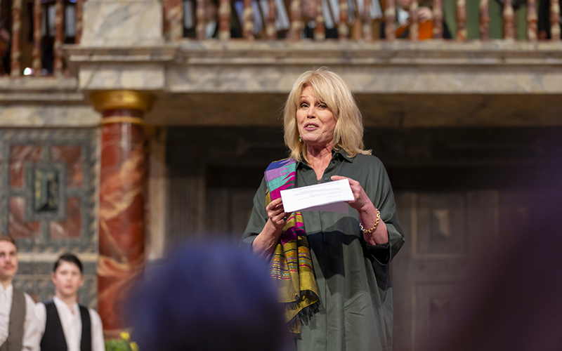 Joanna Lumley Harrow School A woman stands on a stage reading from a piece of paper