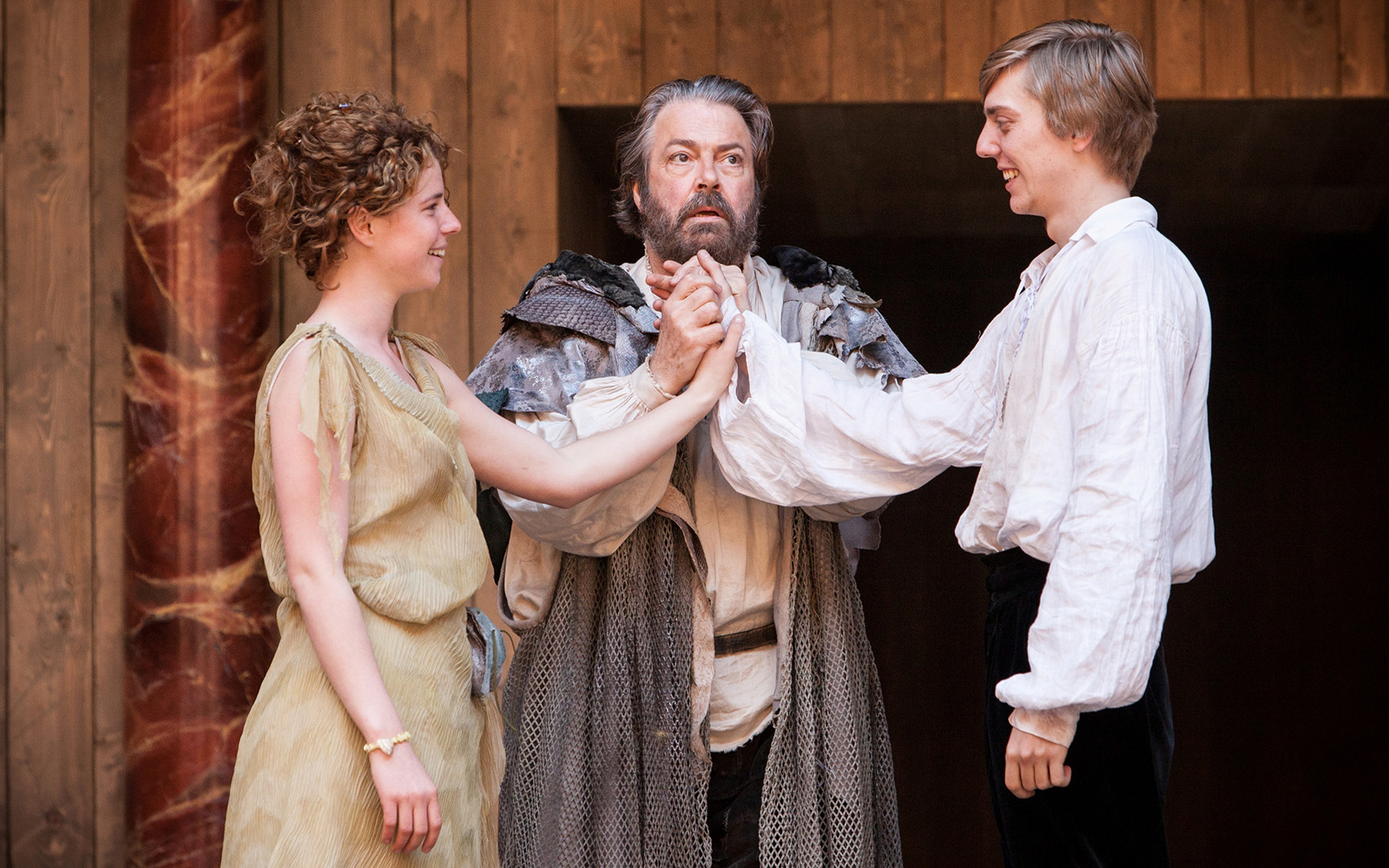 The Tempest Globe Player A man in a grey gown holds a couple's hands together who smile at each other
