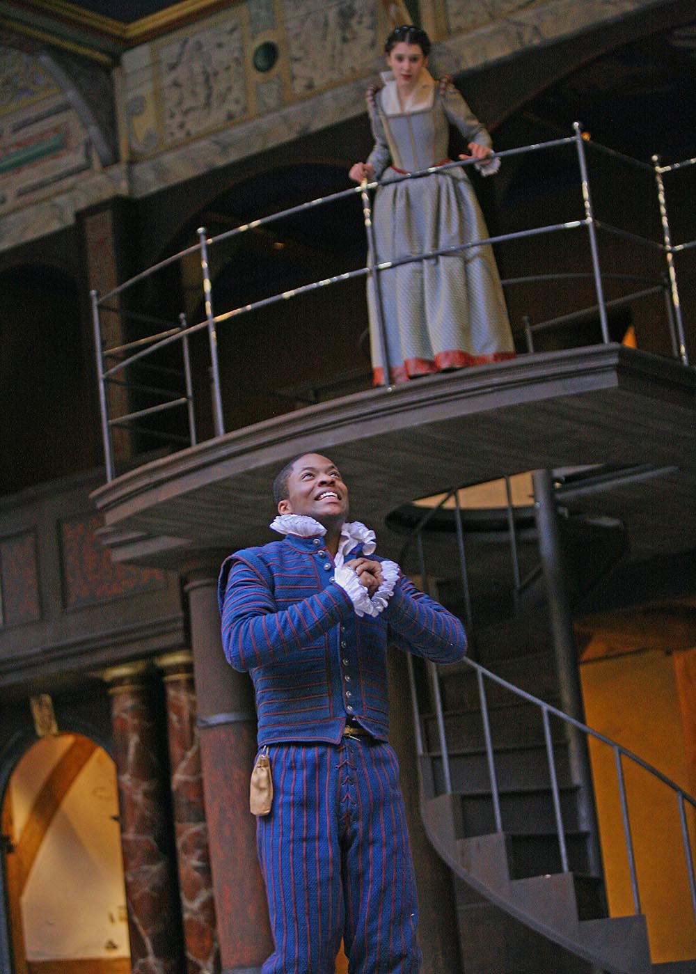 Romeo and Juliet 2009 Young Hearts Season A young woman watches from a balcony as a young man clutches his hands to his chest, besotted.