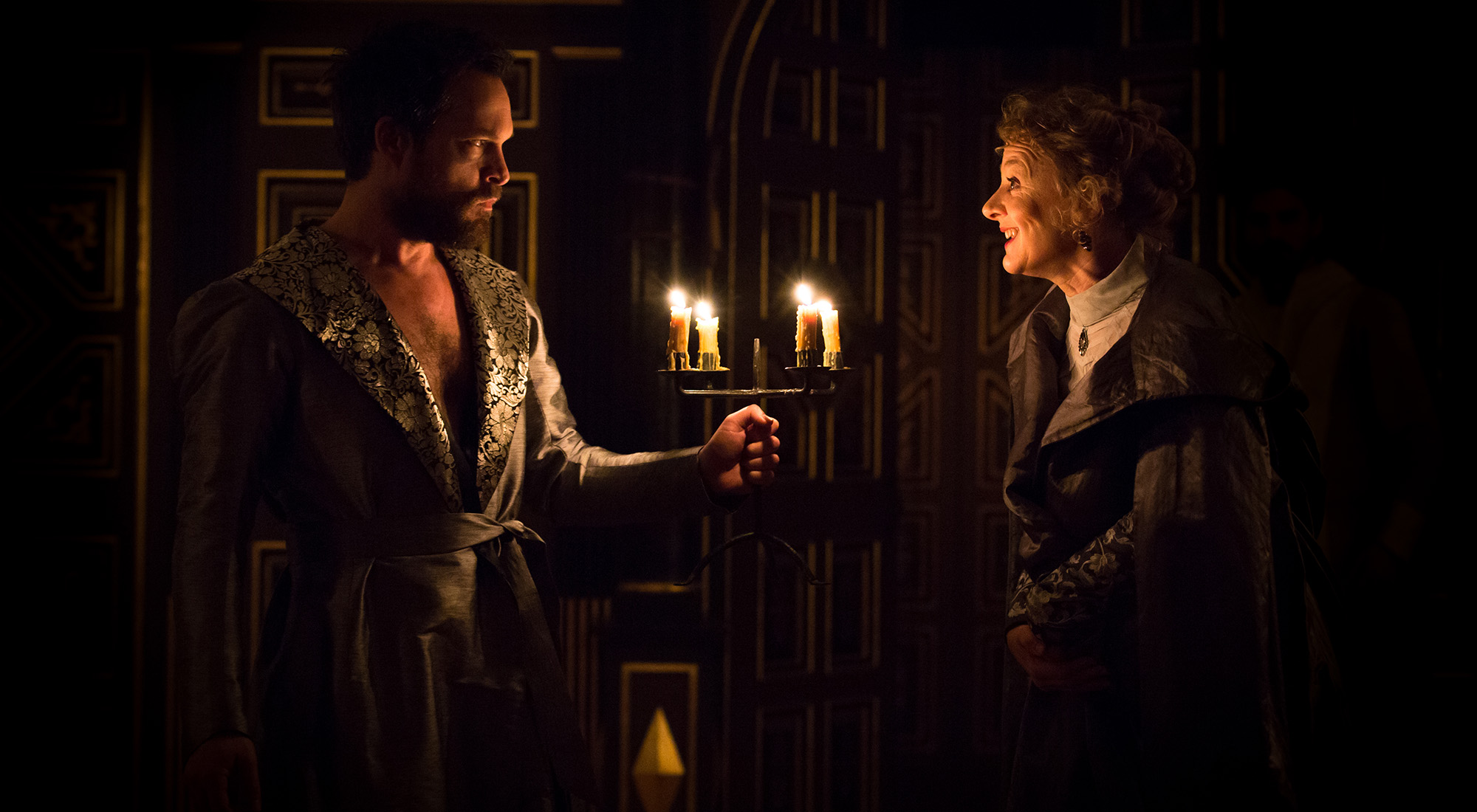 The Winter's Tale Sam Wanamaker Playhouse 2016 A man wearing a dressing robe holds a lit candelabra before a woman who smiles at him.