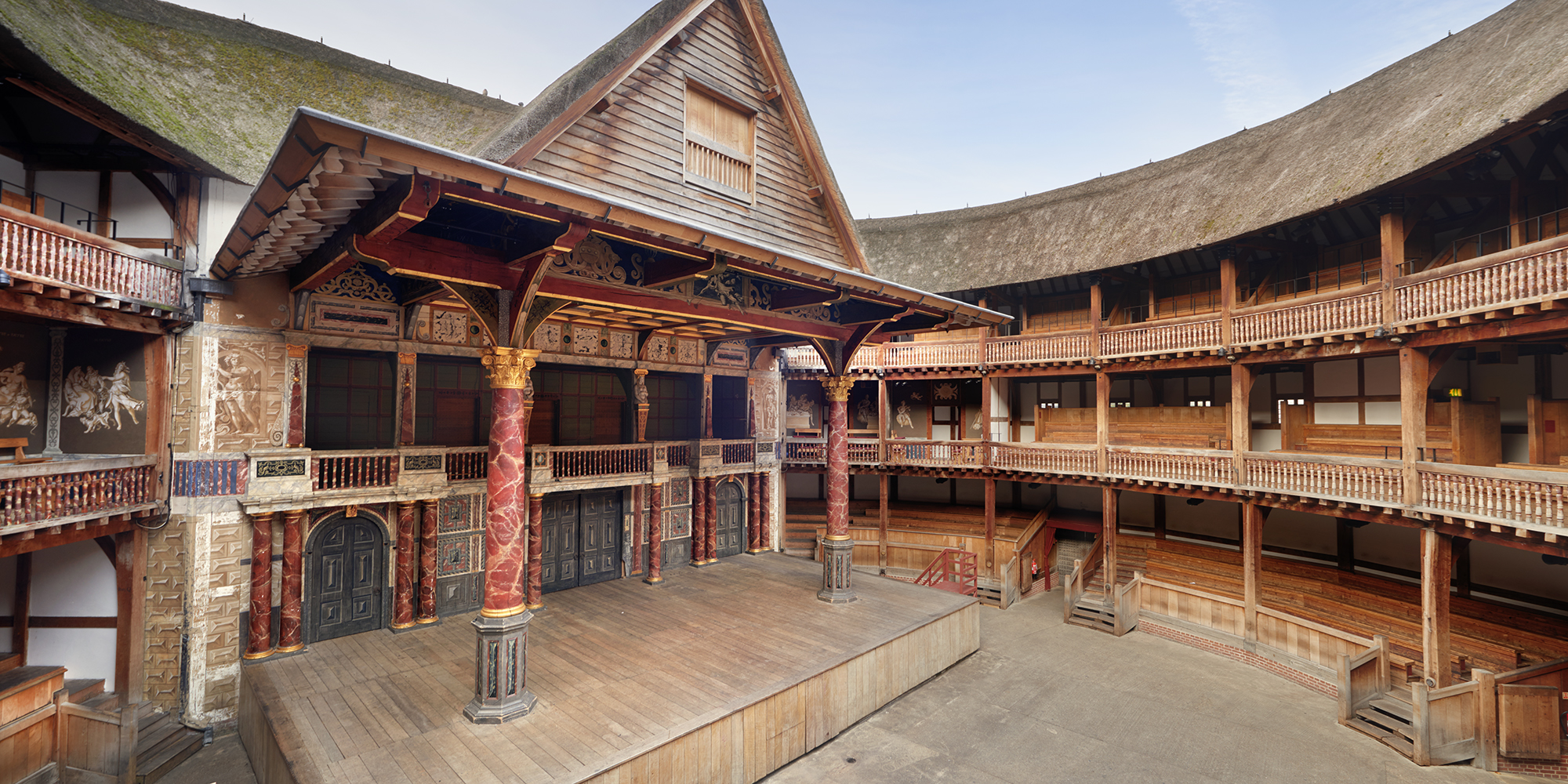 Globe Theatre from lower gallery Shakespeare's Globe Interior shot of a circular timber theatre, with a wooden thrust stage, with two large pillars holding up a thatched roof.