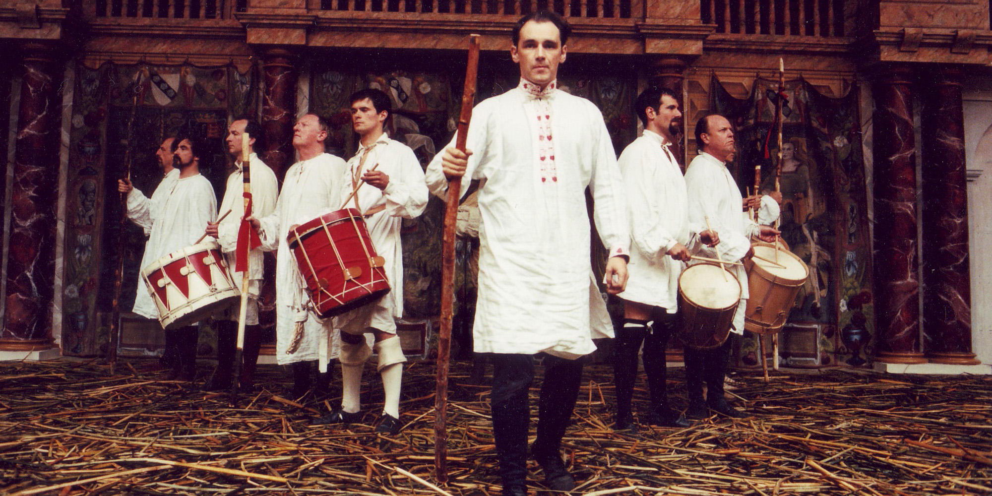 Henry V Globe Theate 1997 Mark Rylance and Company Shakespeare's Globe A group of actors wearing white tunics stand in a v-formation on a stage covered in straw.