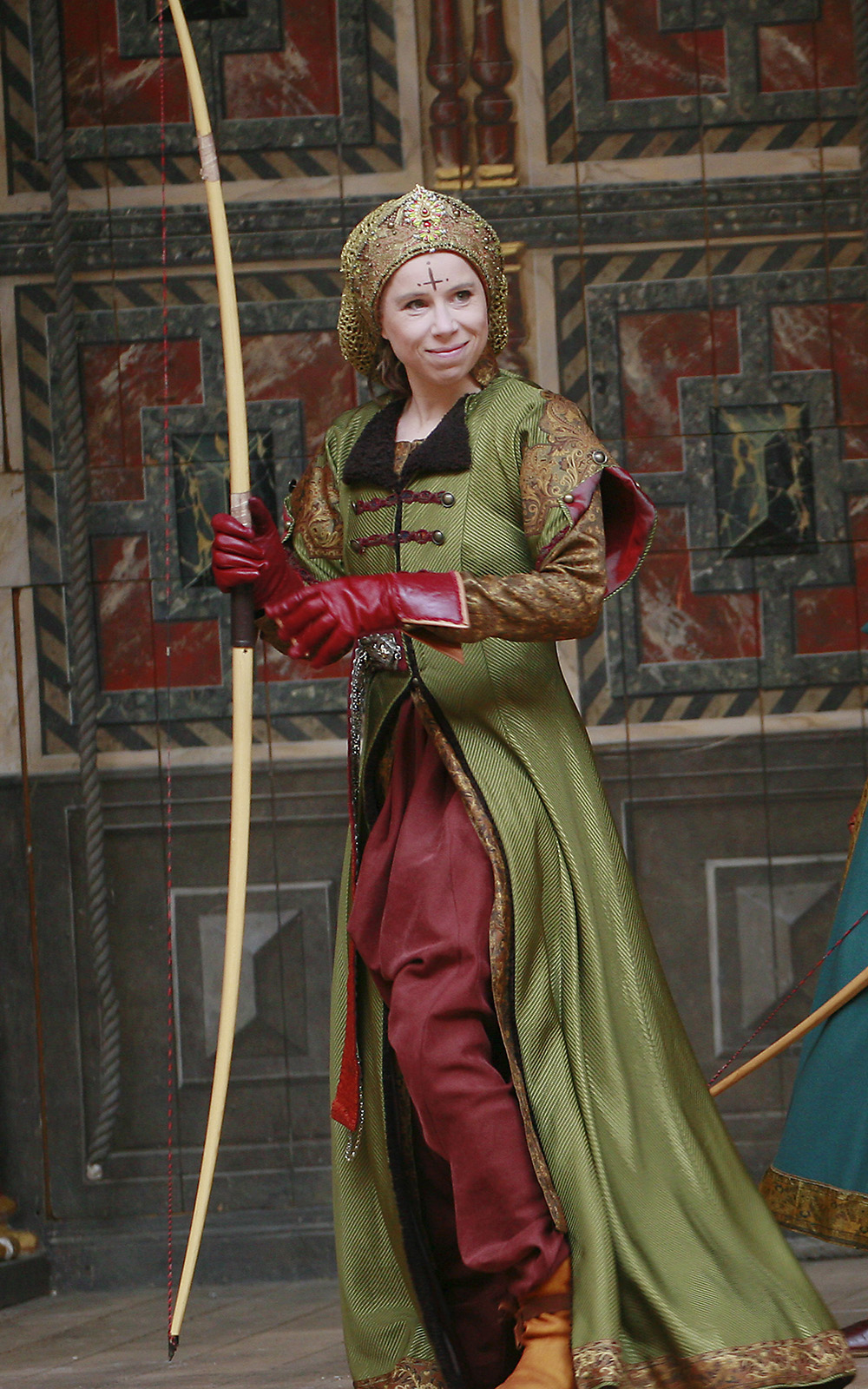 Michelle Terry Hippolyta A Midsummer Night's Dream Shakespeare's Globe An actor wearing a green hunting coat holds a long bow.