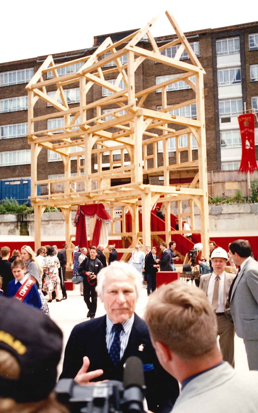 Sam Wanamaker Globe construction Shakespeare's Globe A man stands before a group of people talking, with two wooden bays behind him.