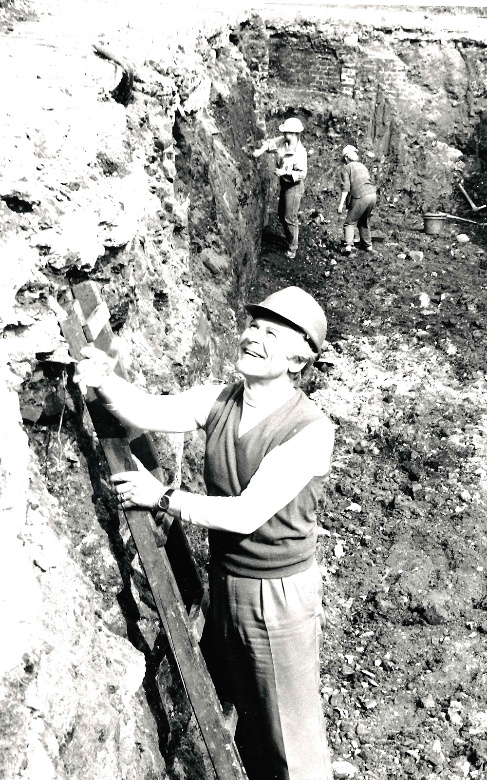 Sam Wanamaker Site Shakespeare's Globe A man stands on a ladder in a ditch of mud and dirt, wearing a hard hat.