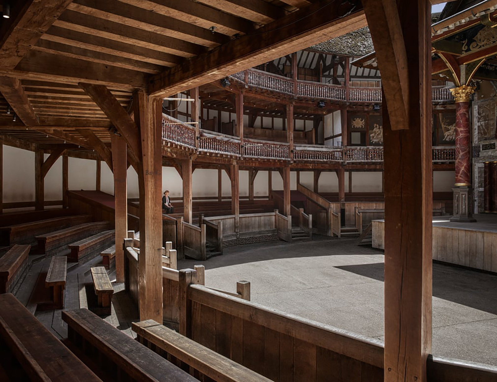 Custodians for Covid Shakespeare's Globe A woman sits in the lower gallery of a circular timber theatre, which lays empty.