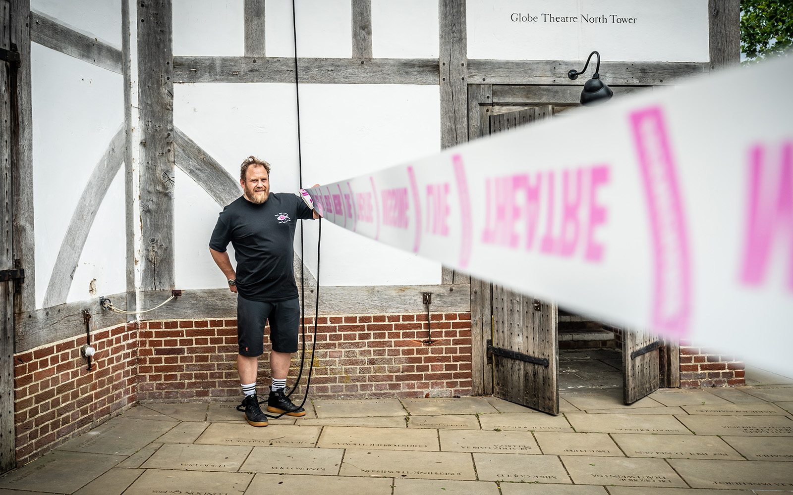 Scene Change Globe-250 A man stands holding one end of a piece of white and pink tape.