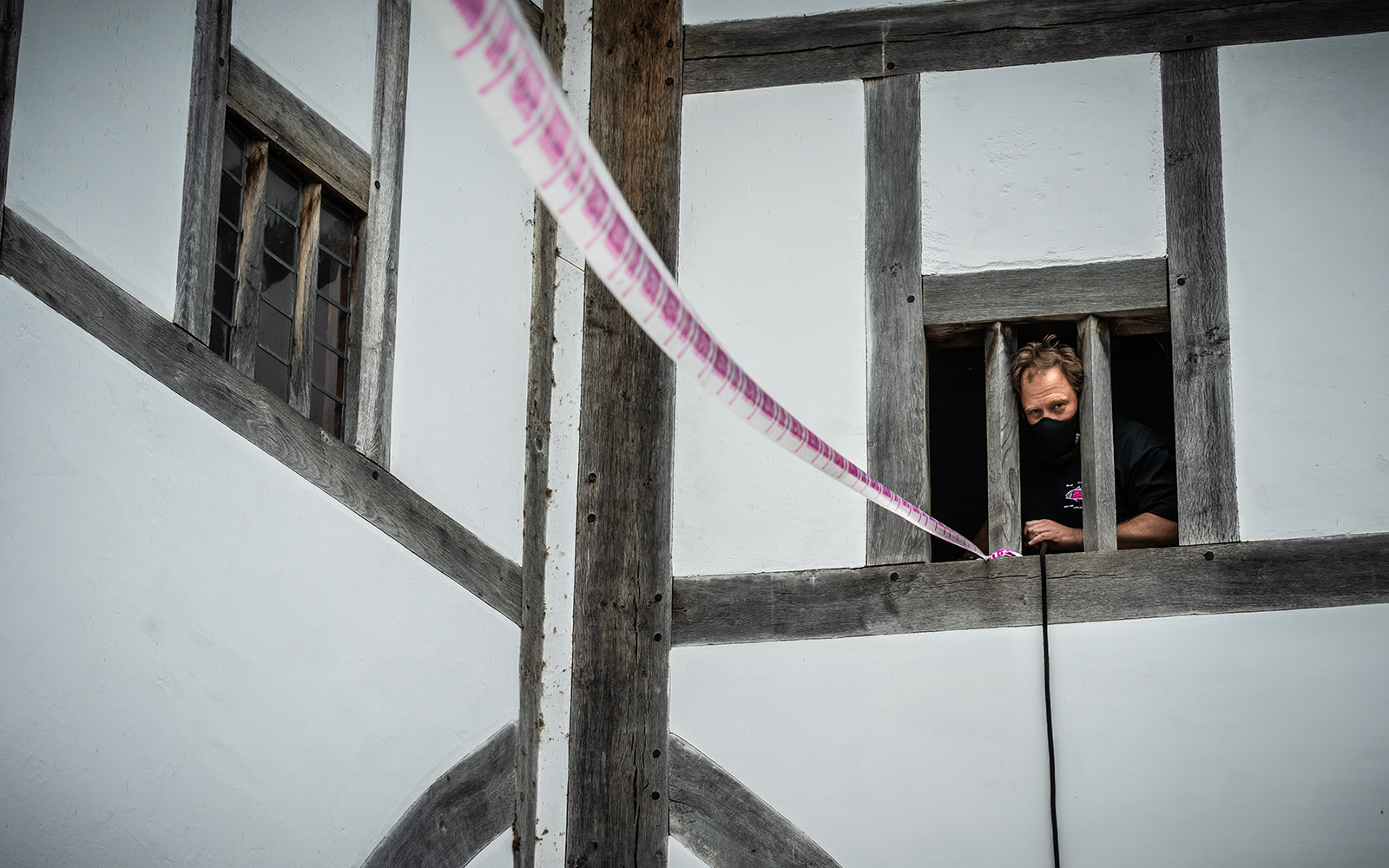 Scene Change Globe-518 A man leans out of a window, fixing a piece of white and pink tape.