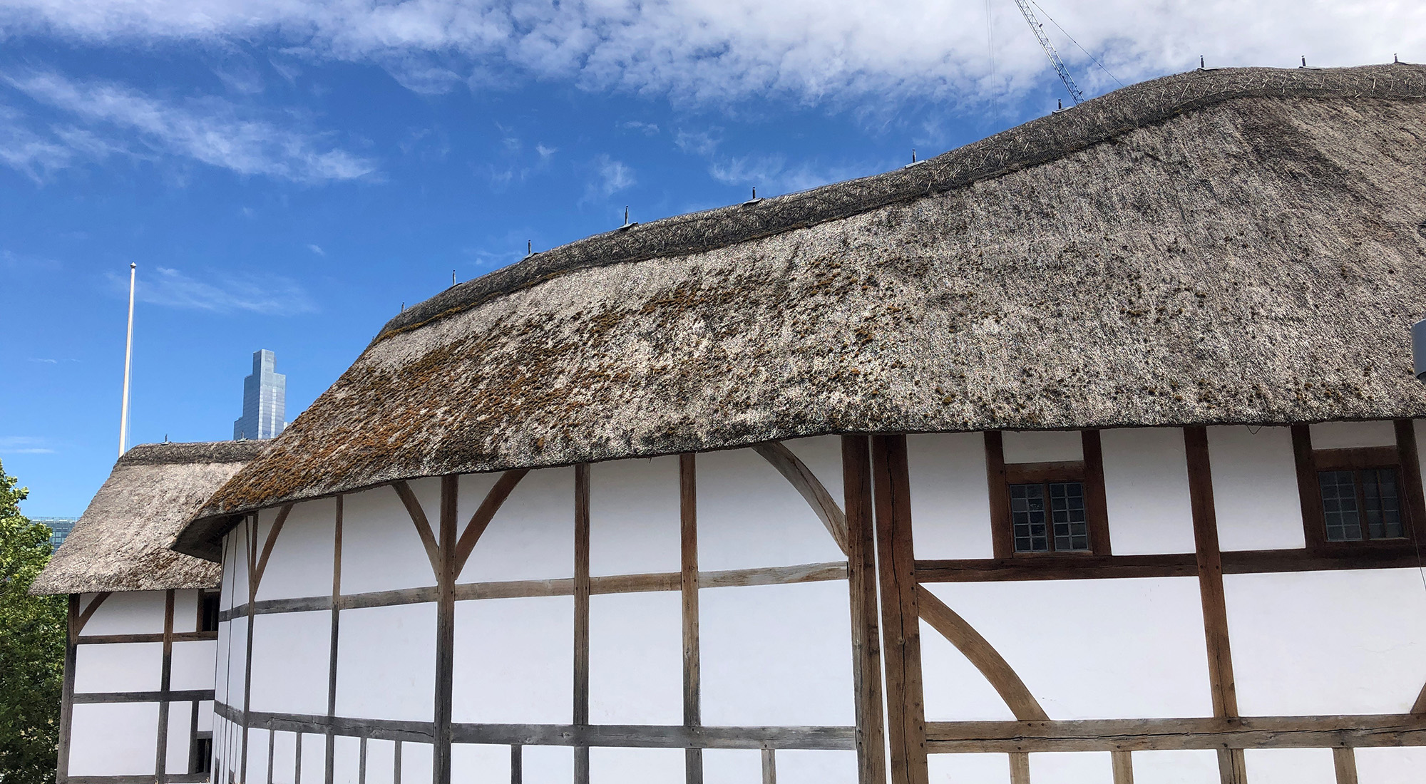 Globe Theatre Summer 2020 Shakespeare's Globe A side view looking at a white wattle and daub theatre, with a blue sky above.