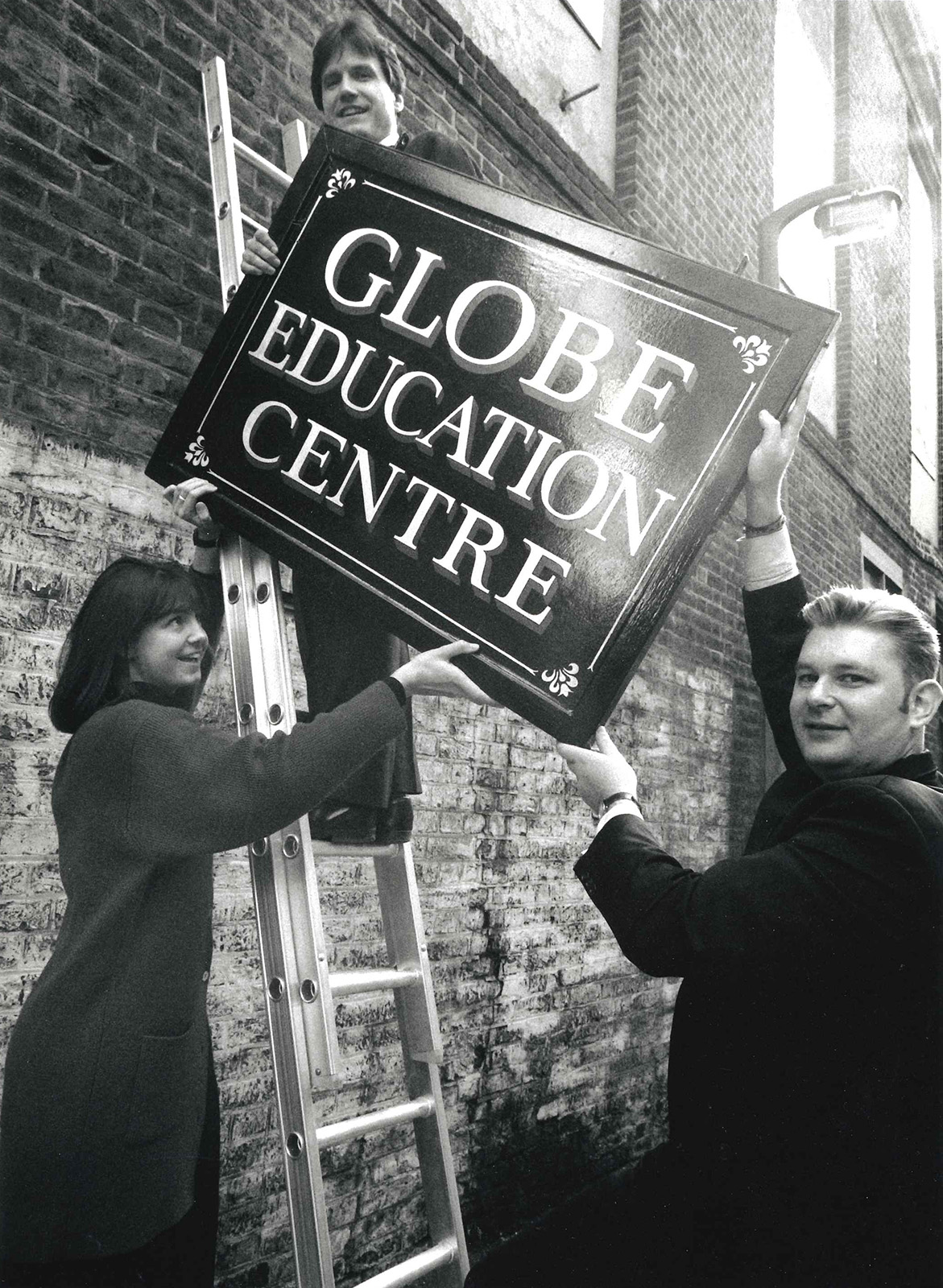 32 Patrick Spottiswoode Installation of the Globe Education Centre sign in 1994 Three people lift a sign saying Globe Education Centre up a ladder.