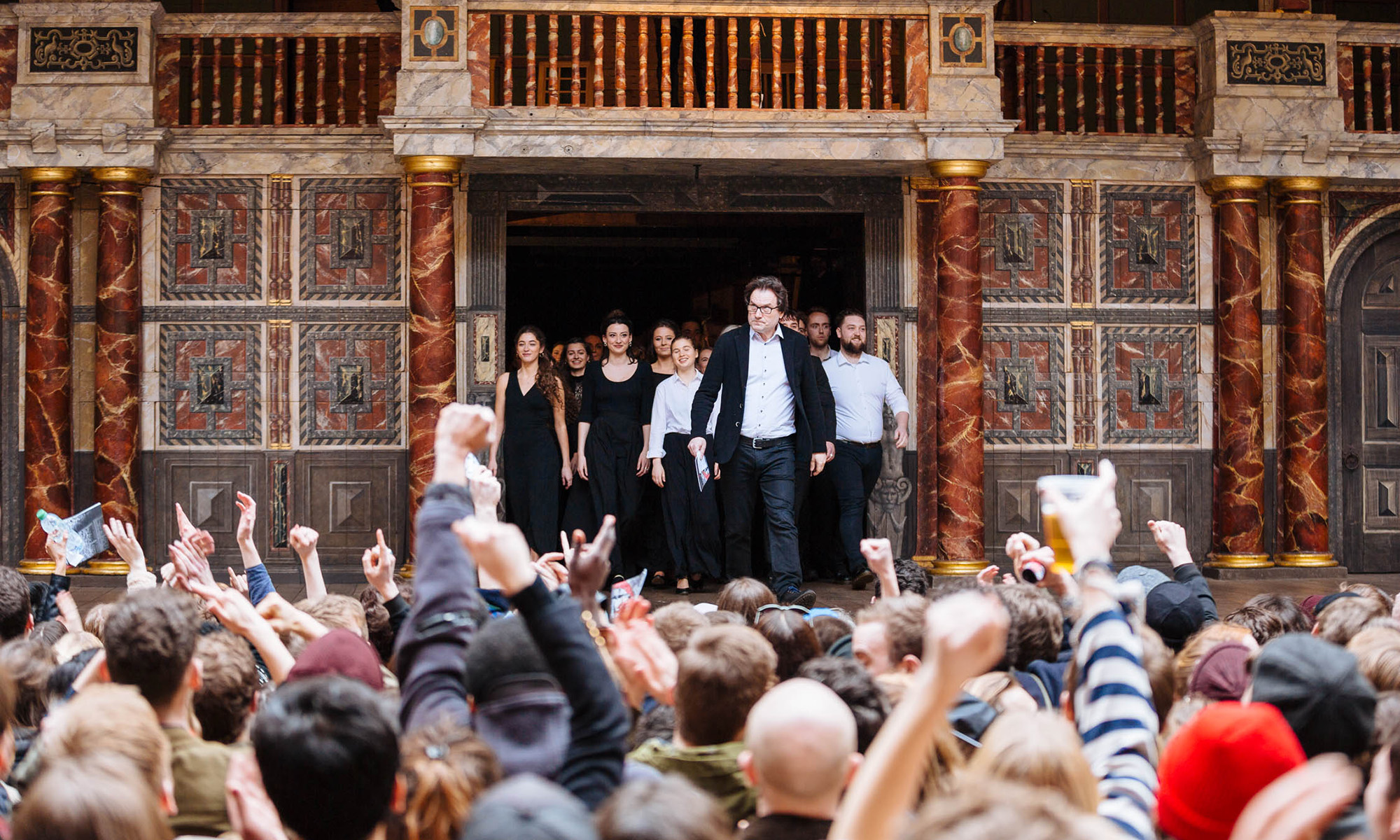 Sam Wanamaker Festival Patrick Spottiswoode 2018 Cesare De Giglio A crowd of people watch as a man leads a group of young actors on to a stage.