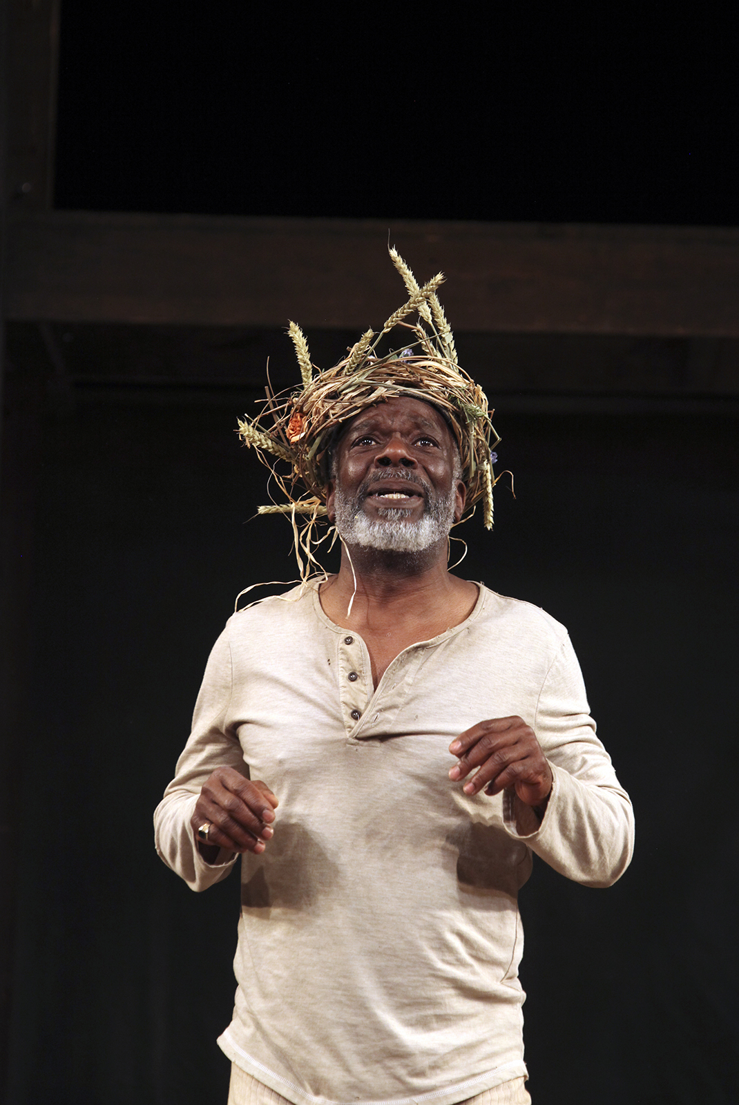 Joseph Marcell King Lear Shakespeare's Globe 2013 Ellie Kurttz A man wearing white undergarments stands dismayed with a wreath of branches on his head.
