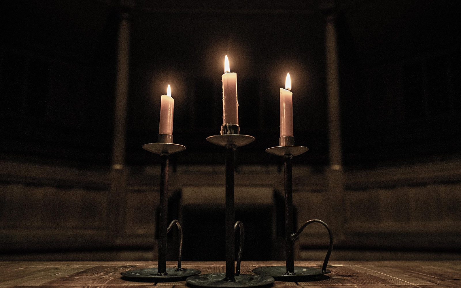 Spooky stories three candles Three lit candles in the dark shadows of an indoor wooden theatre.
