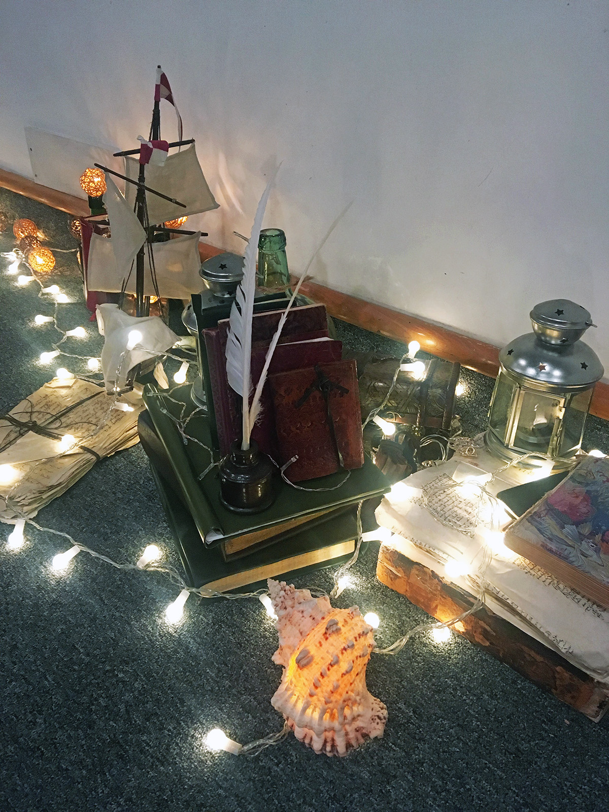 books and light Fairy lights wrap around a pile of books, a model ship and lantern.