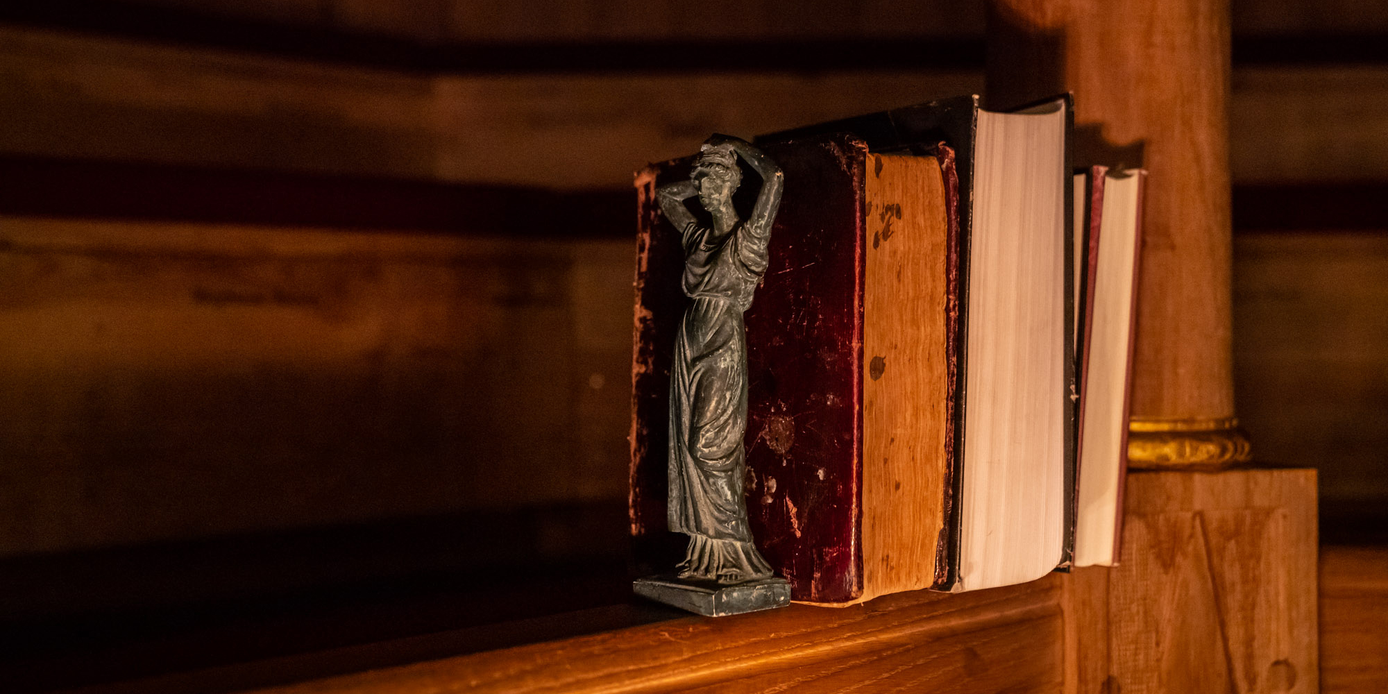 Books Sam Wanamaker Playhouse Marc Brenner A row of books sits on the wooden gallery of the Sam Wanamaker Playhouse, cast in candlelight and shadows.
