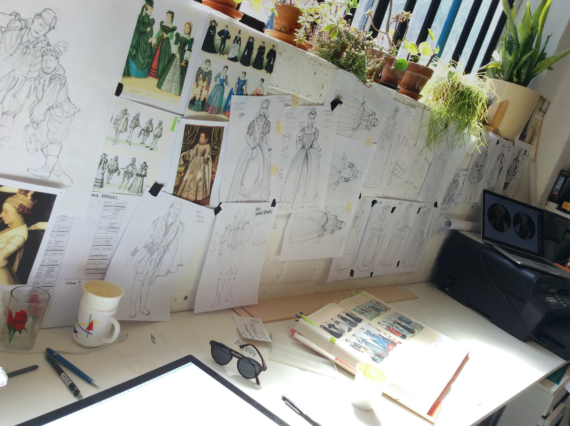 Emilia Costume Sketches Costume Design Jo Scotcher Shakespeare’s Globe A photo of a designer’s desk shows sketches, a sketch book, a mug, a glass and pens